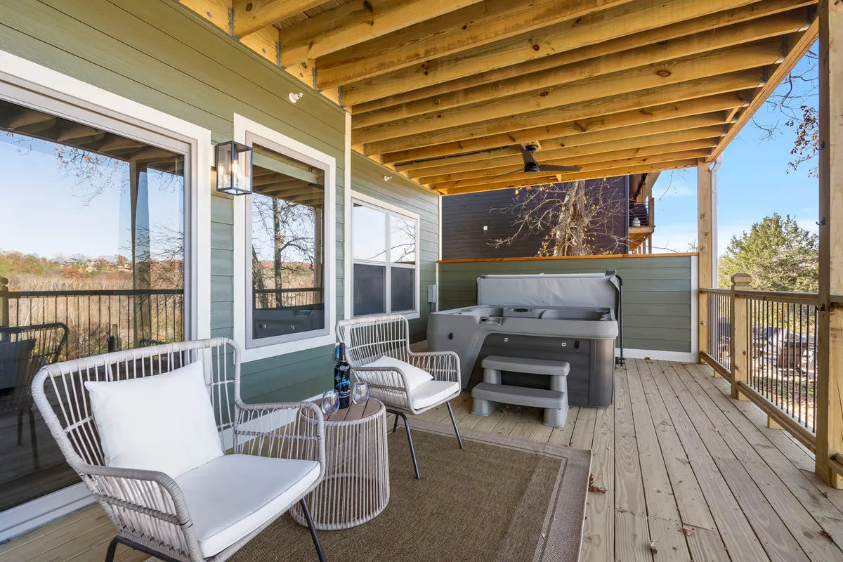This exterior image shows a spacious wooden deck equipped with a private hot tub and comfortable seating, offering an inviting space for relaxation and socializing. The deck overlooks natural surroundings and is perfectly suited for unwinding after a day of adventures or enjoying a morning coffee with a view.