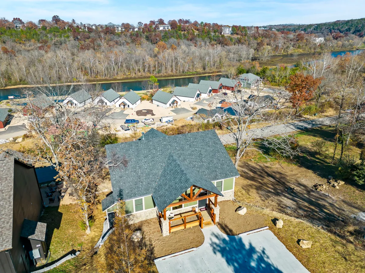 An inviting outdoor seating area is featured next to the main house and riverside cabins, with views of the river and space for outdoor meals or gatherings. The landscape suggests proximity to water activities and trails.
