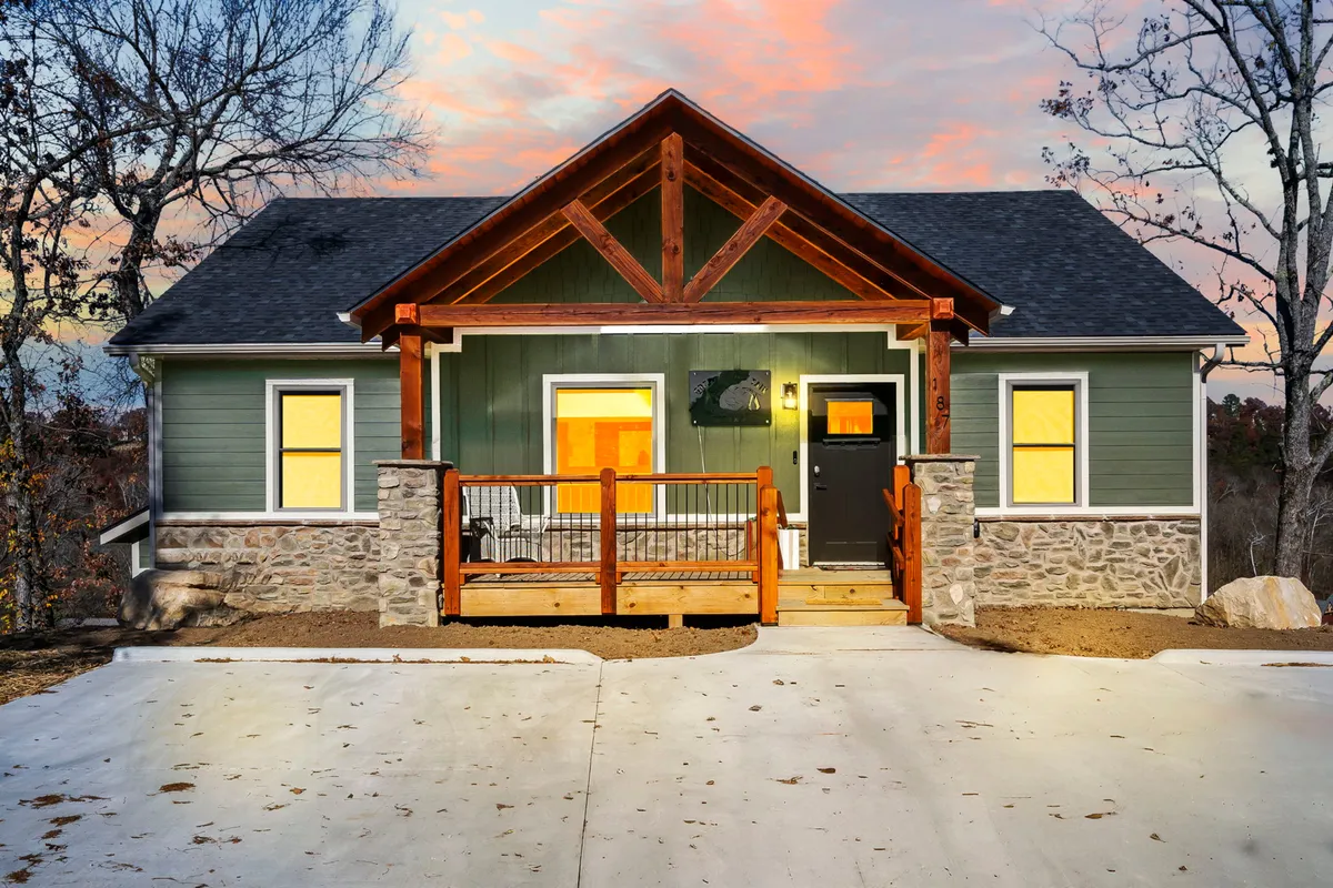 This exterior image showcases the welcoming front porch of Green’s Mountain Getaway, featuring a stone facade, wooden railings, large windows, and exposed beams. The scene suggests a serene spot for relaxing on the porch, enjoying sunset views, or gathering with loved ones.