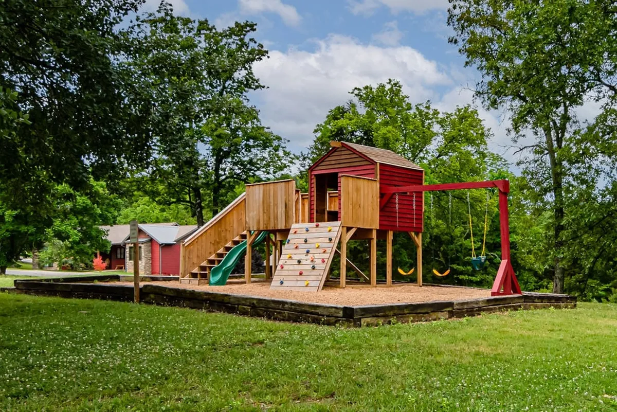 A vibrant play structure featuring a slide, swings, and a climbing wall nestled in an outdoor setting. Children are seen playing, while families can gather for picnics and togetherness, capturing a joyful and active atmosphere.