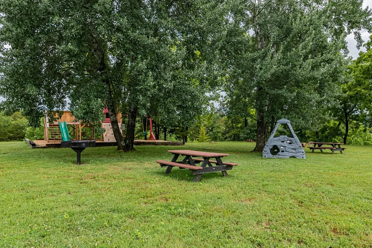 A vibrant playground structure is surrounded by picnic tables, a grill, and a rock climbing feature. The scene is lively and playful, inviting children and families to spend time outdoors together.