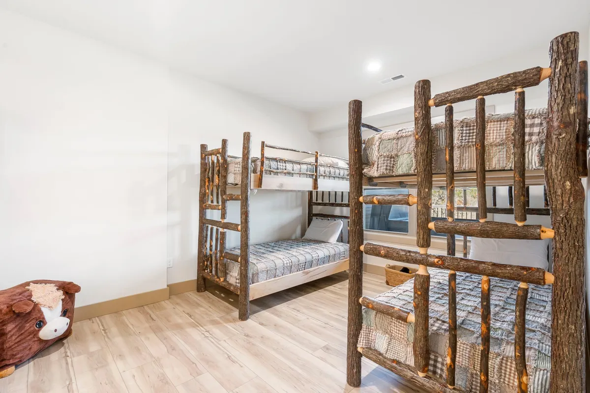 A playful bunk room with natural wood twin-over-twin bunks, soft checkered bedding, and a plush stuffed cow. The space feels inviting and fun, perfect for kids or a group of friends.